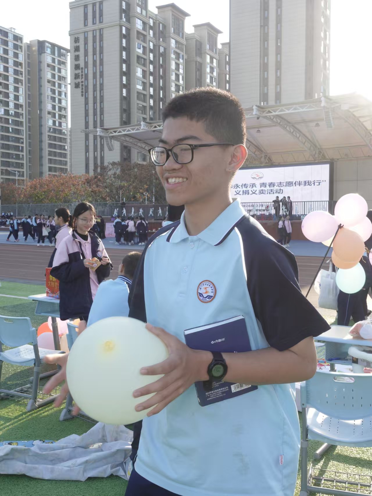 同学手抱气球和书本，开心地参与义卖